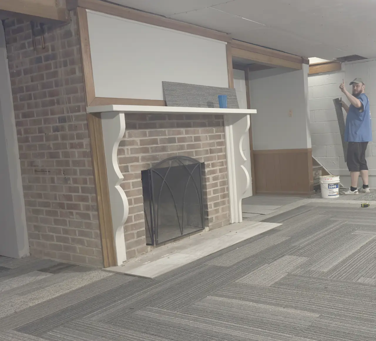 Finished basement with a brick fireplace, painted block walls and carpet tile.